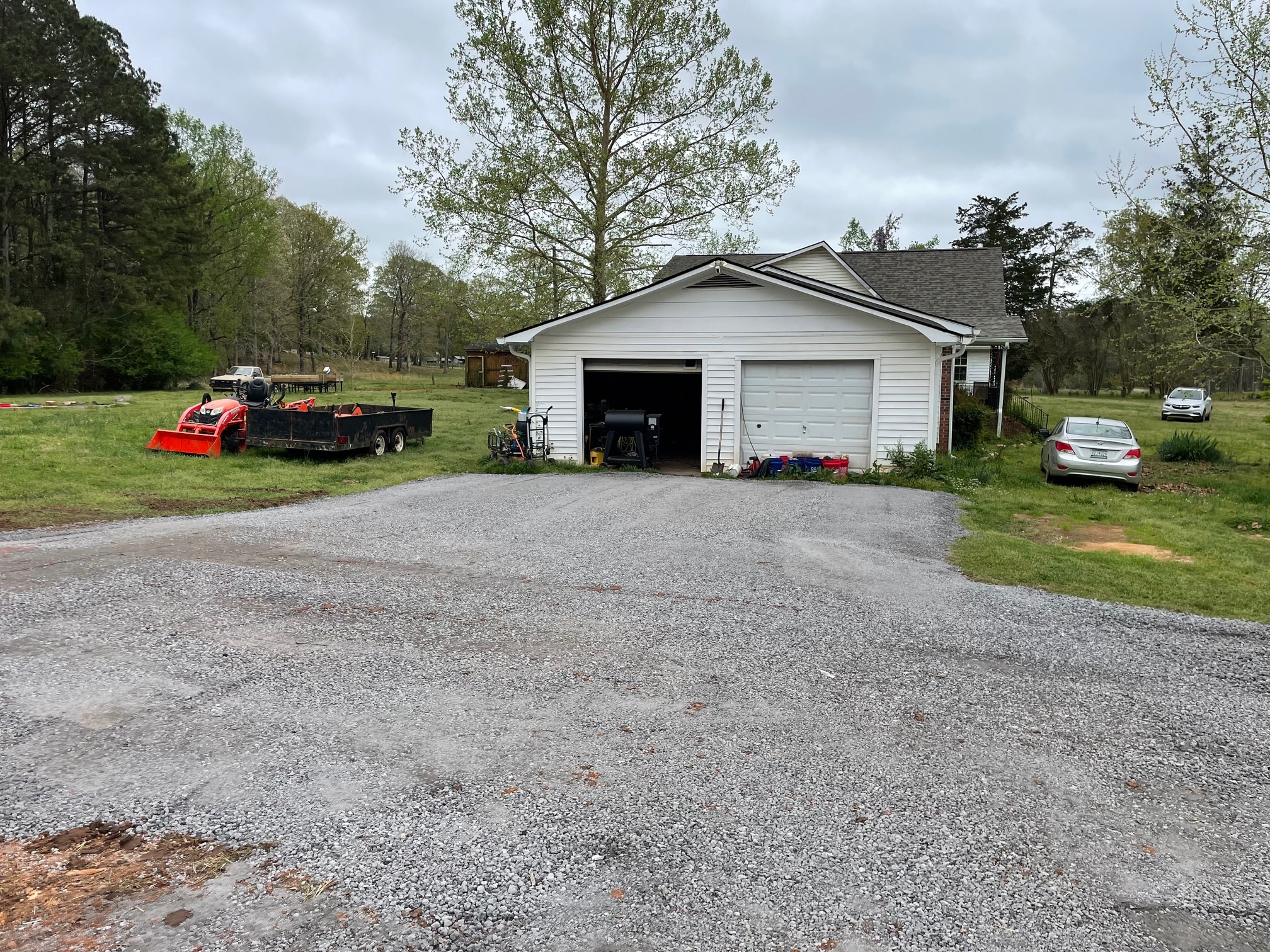 White garage with newly installed gravel driveway and trailer equipment nearby
