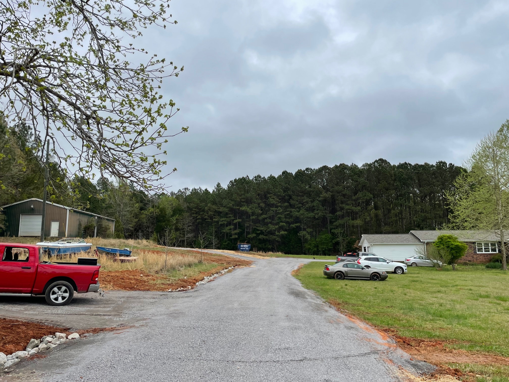 Gravel driveway leading to a home and metal building with vehicles parked on grassy areas